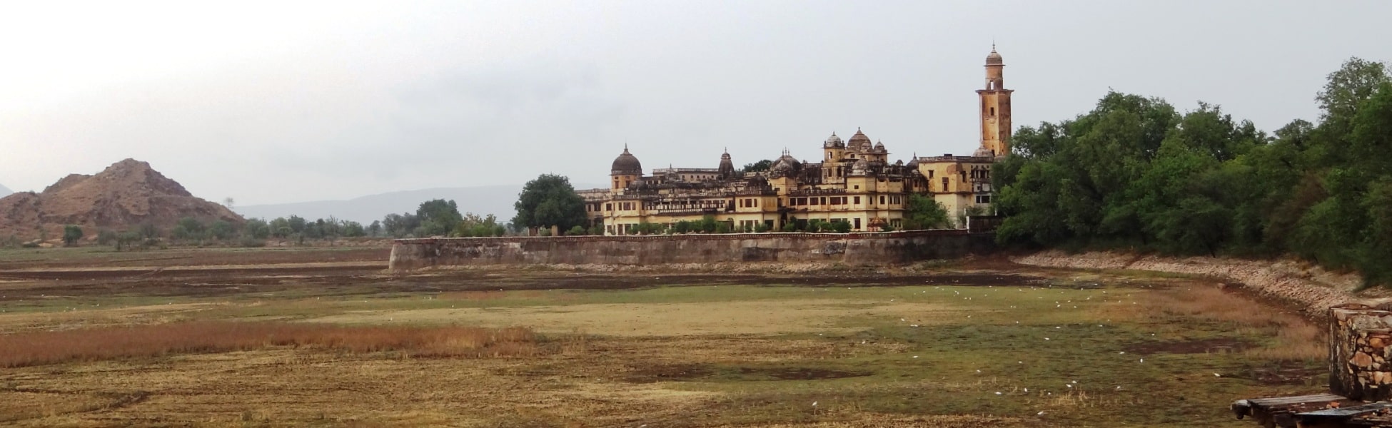 Wide panoramic landscape of the historic yellow stone Vijay Mandir Palace with its grand domes and watchtower, fronted by the grassy dry bed of Vijay Sagar Lake in Alwar, Rajasthan, serving as a vintage cinematic shooting location. film production house in Bandipore, video production house in Bandipore, tv production house in Bandipore, production house in Bandipore, film production company in Bandipore, video production company in Bandipore, tv production company in Bandipore, production company in Bandipore