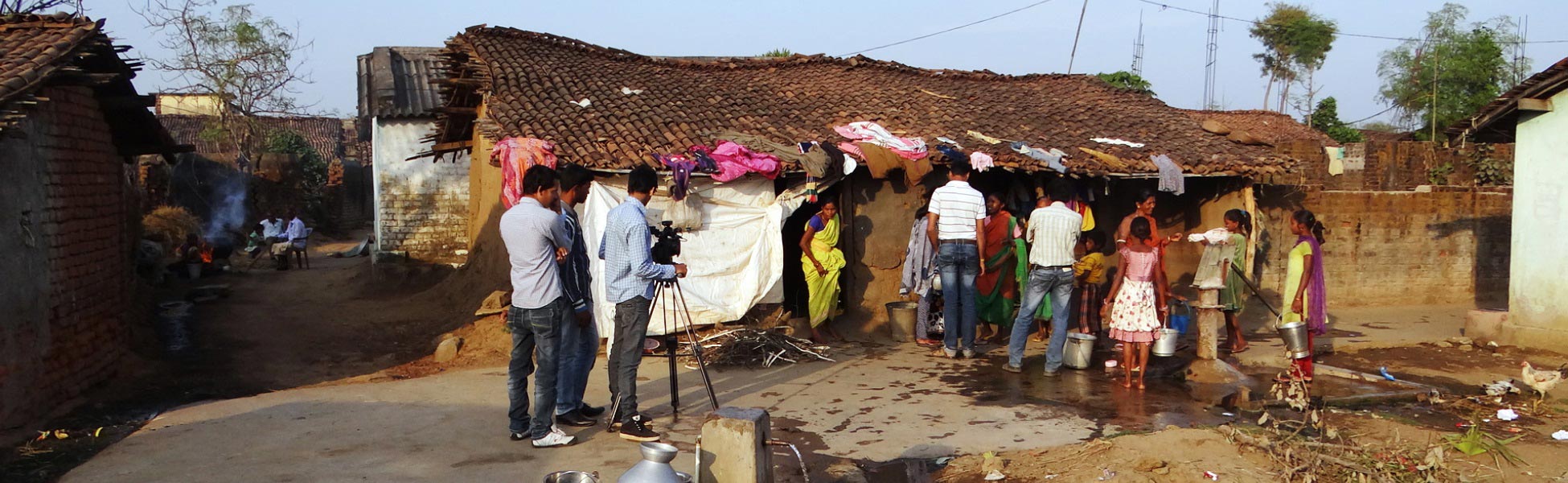 A professional video production crew filming a social impact documentary on location in a rural village in Bhawanipatna, Kalahandi, Odisha, showing filmmakers with a camera tripod interacting with local residents. film production house in Bangalore Rural, video production house in Bangalore Rural, tv production house in Bangalore Rural, production house in Bangalore Rural, film production company in Bangalore Rural, video production company in Bangalore Rural, tv production company in Bangalore Rural, production company in Bangalore Rural