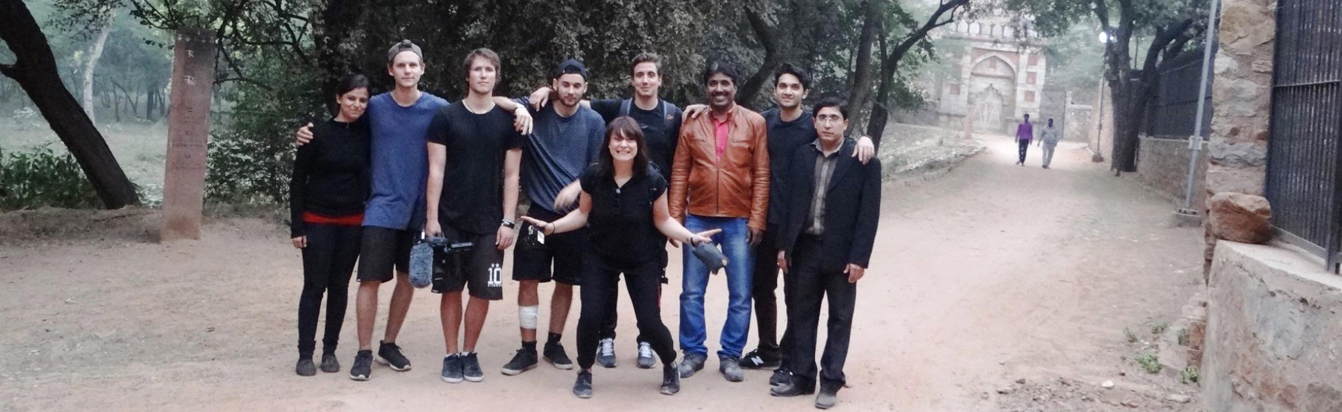 Group photo of the Trisna Films® local team and visiting UK film crew on location in New Delhi, India. The team is posing with camera and audio equipment near a historic archway during the production of Insight TV's adventure documentary series, 'Running The World'. film shooting locations in india