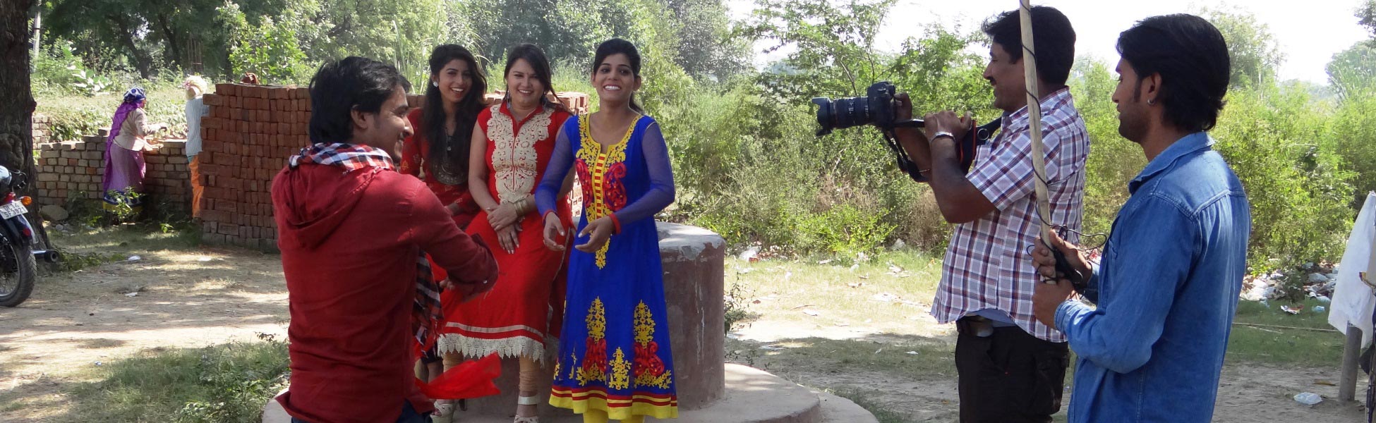 Behind-the-scenes view of an Indian short film production titled 'Don't Harass the Girl' in Ghaziabad, Uttar Pradesh. A videographer captures a scene featuring actors outdoors, including a man on a motorcycle looking toward a group of women in traditional attire. fixer in ramanagara, fixer in Bangalore South, film fixer in ramanagara, film fixer in bangalore south, media fixer in ramanagara, media fixer in bangalore south, movie fixer in ramanagara, movie fixer in bangalore south, production fixer in ramanagara, production fixer in bangalore south, line producer in Bangalore South