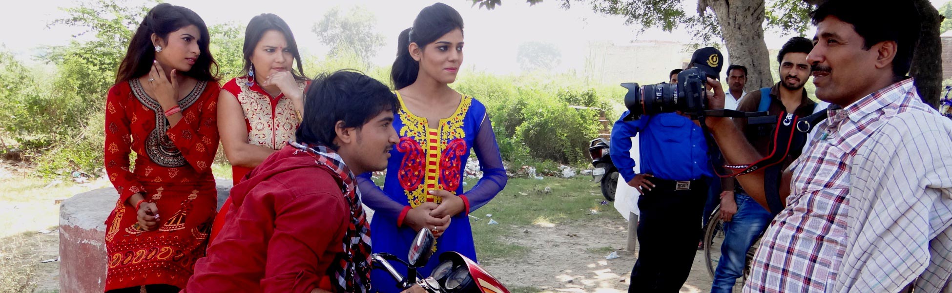 Behind-the-scenes view of an Indian short film crew filming a scene outdoors in Ghaziabad. A videographer uses a DSLR camera setup to film actors on a motorcycle and women in traditional attire. film production house in Bankura, video production house in Bankura, tv production house in Bankura, production house in Bankura, film production company in Bankura, video production company in Bankura, tv production company in Bankura, production company in Bankura