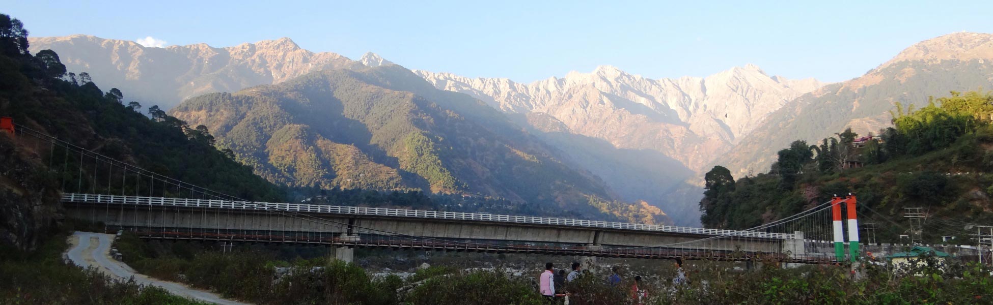 A wide panoramic view of the rugged Dhauladhar mountain range rising behind a long concrete and suspension bridge at Saurabh Van Vihar in Palampur, Himachal Pradesh, India. film shooting locations in Bankura, video shooting locations in Bankura, tv shooting locations in Bankura, shooting locations in Bankura