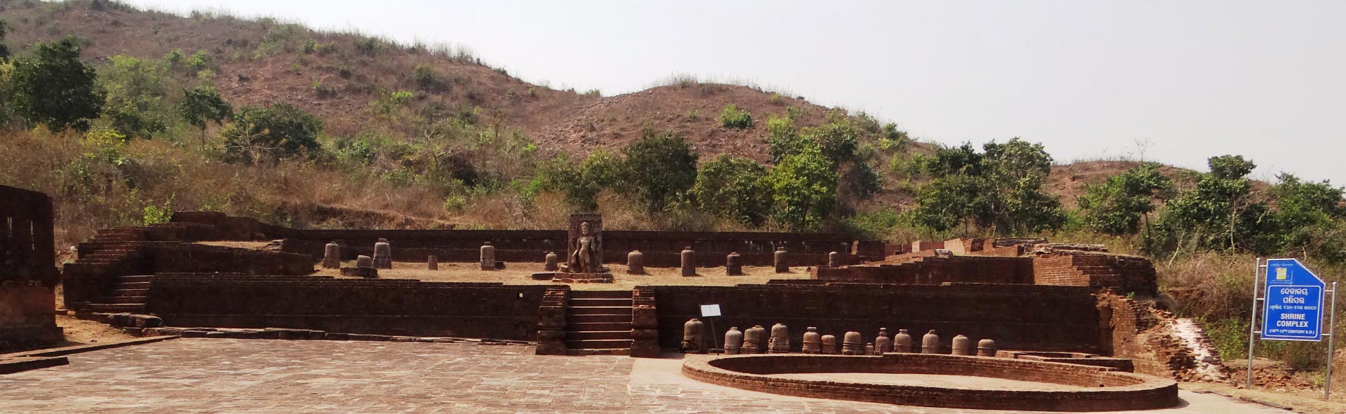 Excavated 10th to 12th-century brick shrine complex at Udayagiri Buddhist site in Jajpur, Odisha, India, featuring a central stone deity sculpture, multiple stone votive stupas on a terraced platform, and a hillside backdrop. film production house in Baramulla, video production house in Baramulla, tv production house in Baramulla, production house in Baramulla, film production company in Baramulla, video production company in Baramulla, tv production company in Baramulla, production company in Baramulla