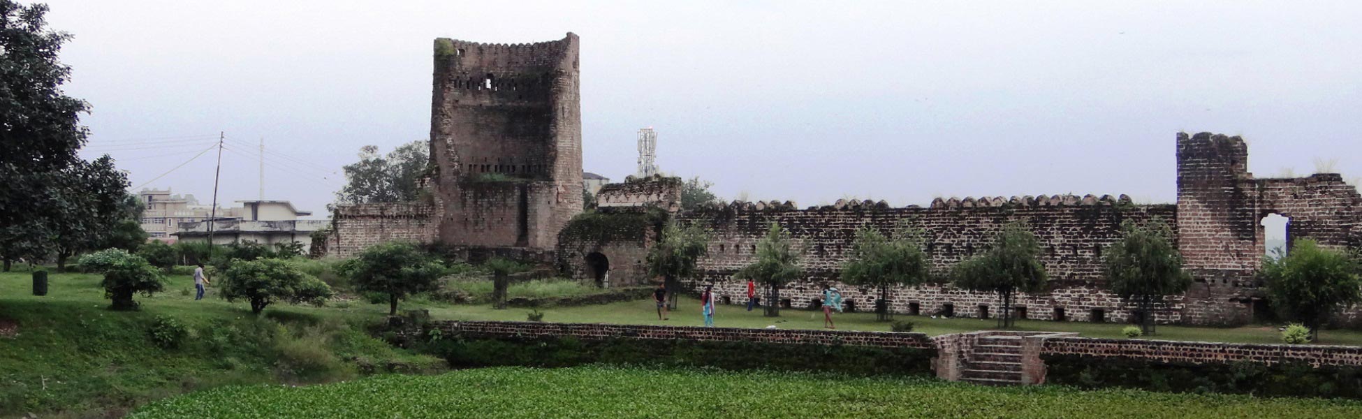 The ancient red-brick fortification wall and rectangular defensive watchtower of Nurpur Fort in Kangra, Himachal Pradesh, with stone paths overlooking a sunken dry moat area. film shooting locations in Barwani, video shooting locations in Barwani, tv shooting locations in Barwani, shooting locations in Barwani