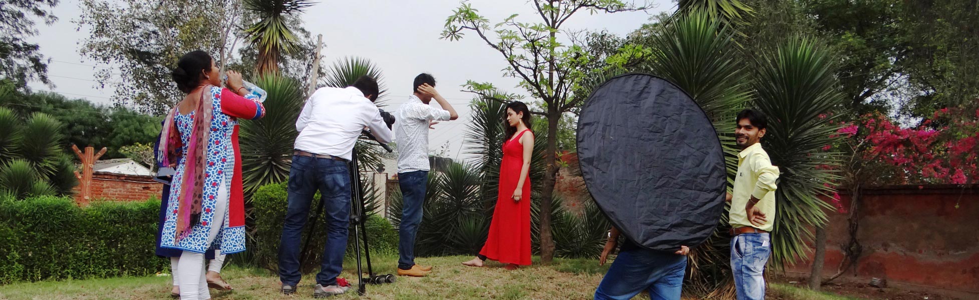 Behind-the-scenes of a music video production in Delhi by Trisna Films, showing a camera operator with a tripod, director coordinating, and an actress in a red dress during an outdoor shoot with lighting reflectors. film production house in Bastar, film production house in jagdalpur, video production house in Bastar, video production house in jagdalpur, tv production house in Bastar, tv production house in jagdalpur, production house in Bastar, production house in jagdalpur, film production company in Bastar, film production company in jagdalpur, video production company in Bastar, video production company in jagdalpur, tv production company in Bastar, tv production company in jagdalpur, production company in Bastar, production company in jagdalpur