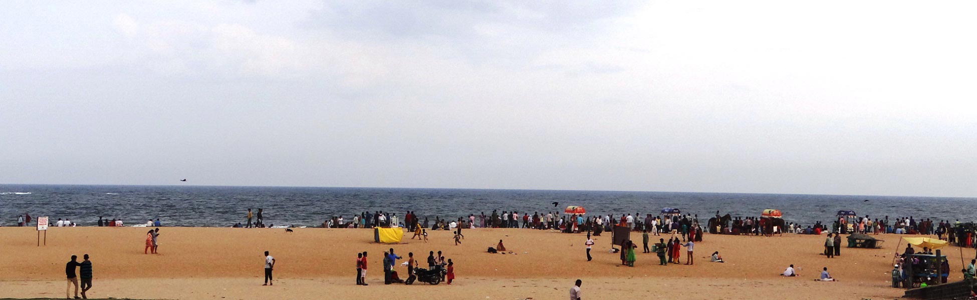 Wide panoramic view of the sandy shoreline at Marina Beach in Chennai, featuring local crowds, small beach stalls, and the ocean under an open sky; an active location scout reference for line production and film crowd management in Tamil Nadu. film shooting locations in Bathinda, video shooting locations in Bathinda, tv shooting locations in Bathinda, shooting locations in Bathinda