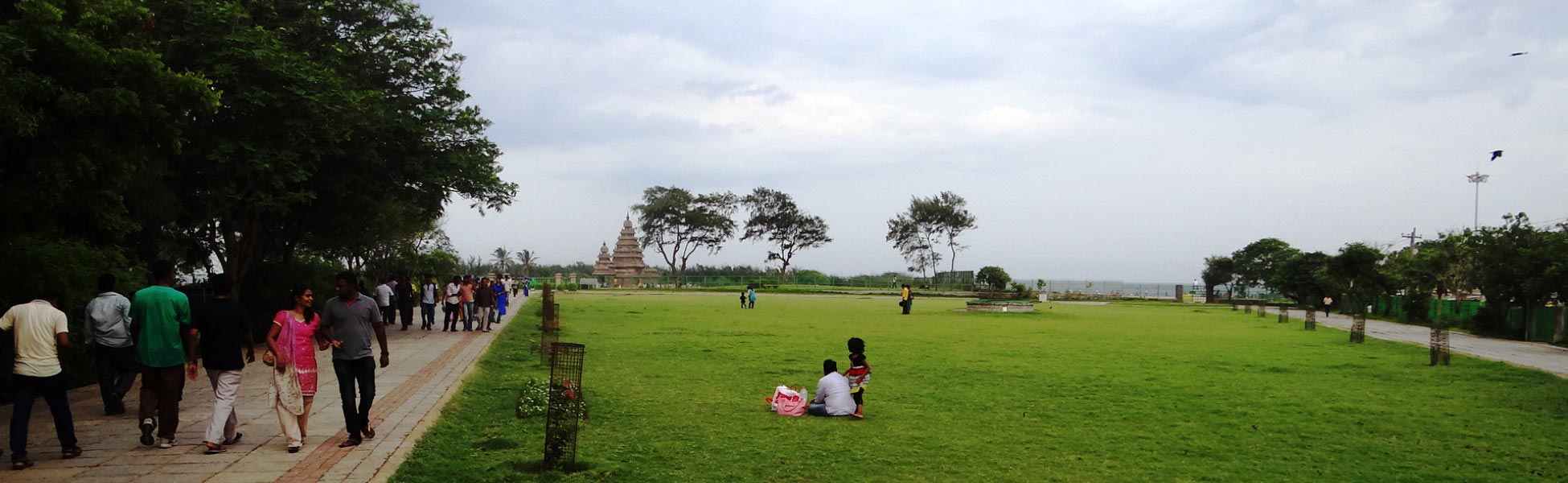 A wide-angle landscape view of the historic 8th-century Dravidian granite Shore Temple in Mahabalipuram, showing visitors on the paved pathway and an expansive green lawn under an overcast sky, ideal for large-scale cinematic set placement. fixer in Beau Bassin - Rose Hill, film fixer in Beau Bassin - Rose Hill, media fixer in Beau Bassin - Rose Hill, movie fixer in Beau Bassin - Rose Hill, production fixer in Beau Bassin - Rose Hill, line producer in Beau Bassin - Rose Hill