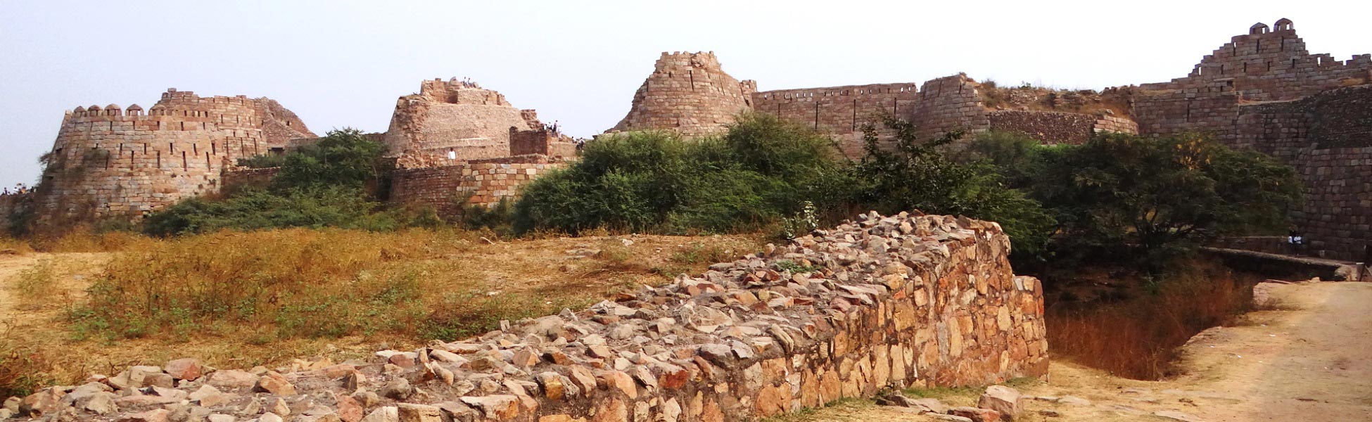 Panoramic view of 14th-century grey quartzite stone bastions, sloping fortification walls, and ancient ruins of Tughlaqabad Fort in South Delhi, ideal for period film shooting and documentary location scouting. fixer in Bemetara, film fixer in Bemetara, media fixer in Bemetara, movie fixer in Bemetara, production fixer in Bemetara, line producer in Bemetara