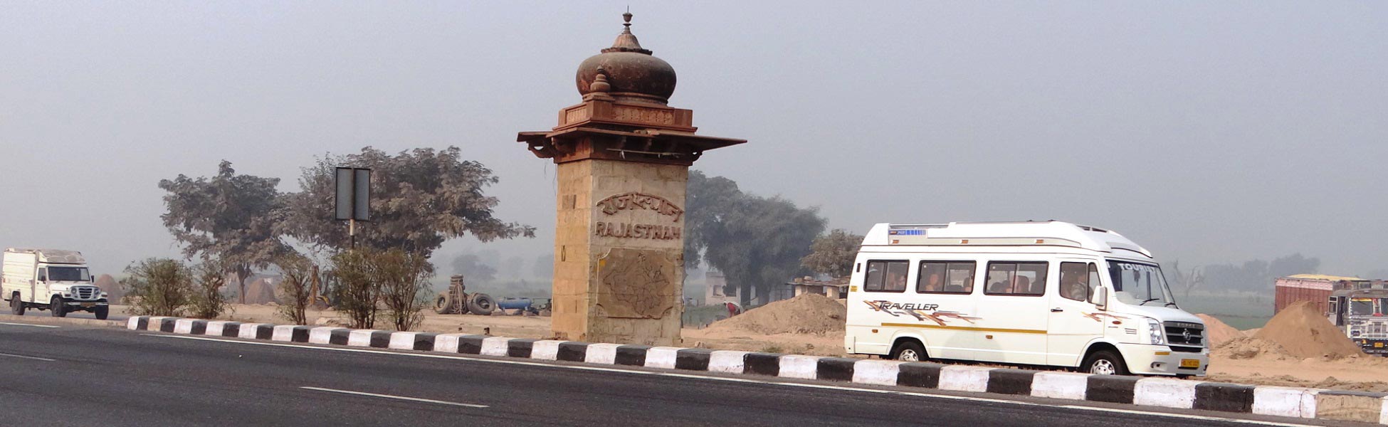 Sandstone welcome pillar with carved map marking the entry into Rajasthan state along the highway, featuring a production crew transit van on the border road. fixer in Bengaluru Urban, film fixer in Bengaluru Urban, media fixer in Bengaluru Urban, movie fixer in Bengaluru Urban, production fixer in Bengaluru Urban, line producer in Bengaluru Urban