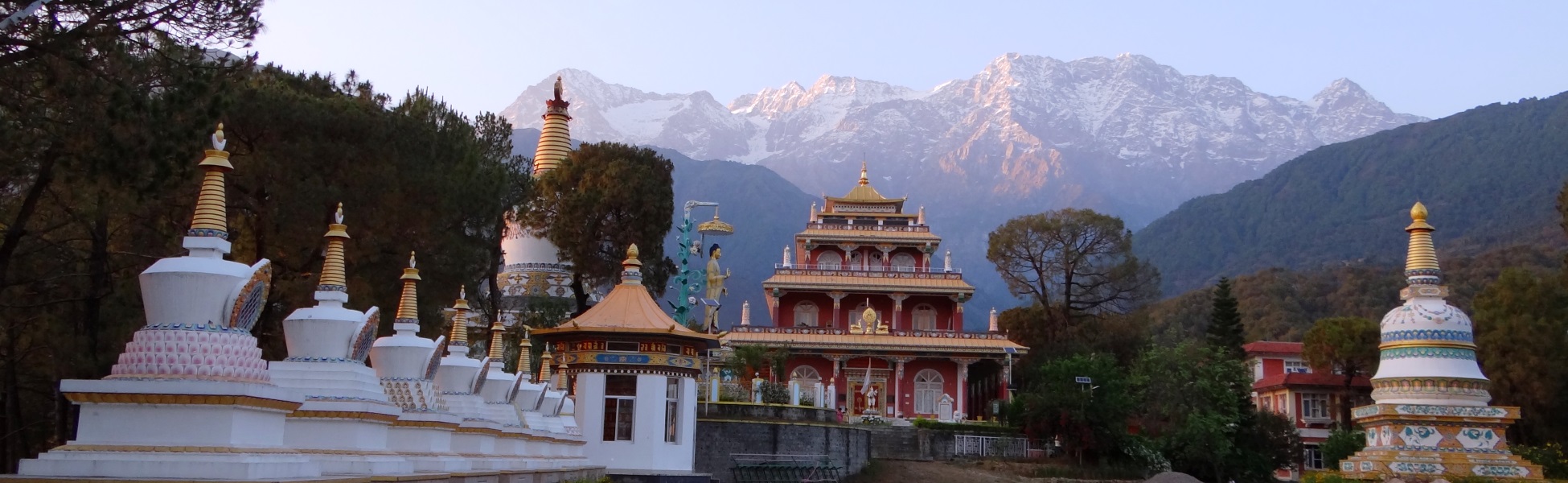 White Tibetan Buddhist stupas and red temple at Tashi Jong Monastery in Kangra Valley, framed by the snow-capped Dhauladhar mountains. film shooting locations in Betul, video shooting locations in Betul, tv shooting locations in Betul, shooting locations in Betul