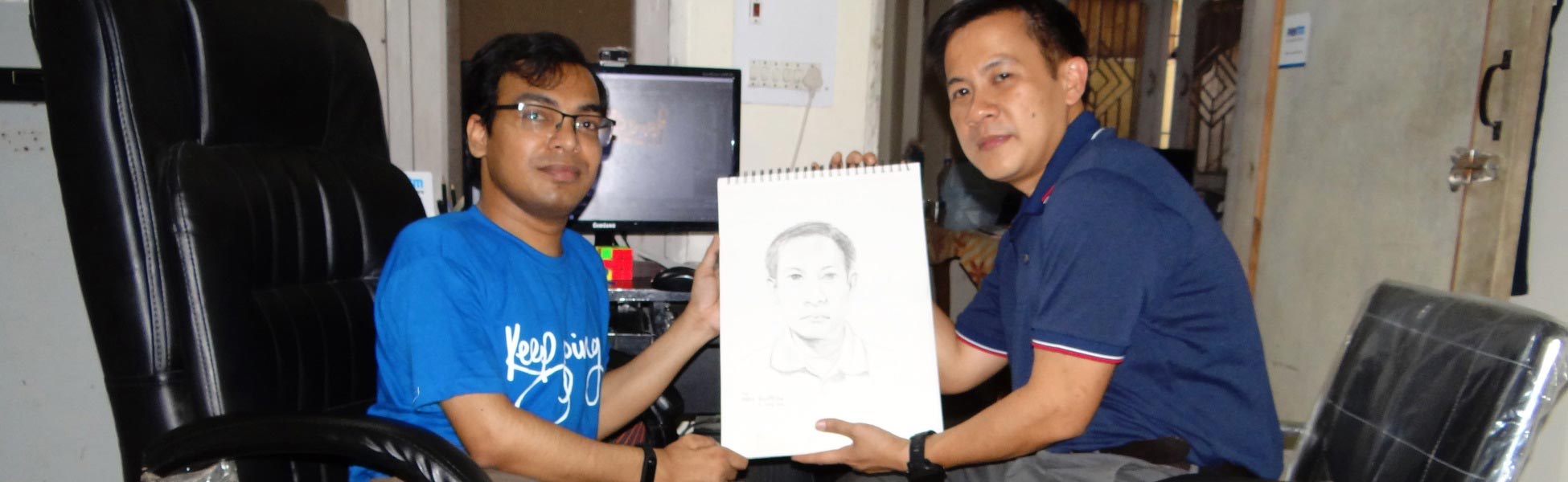 Artist Kamal Nishad smiling alongside a client in a studio while together holding a framed 1-minute hand-drawn pencil portrait sketch. film shooting locations in bhagalpur, video shooting locations in bhagalpur, tv shooting locations in bhagalpur, shooting locations in bhagalpur