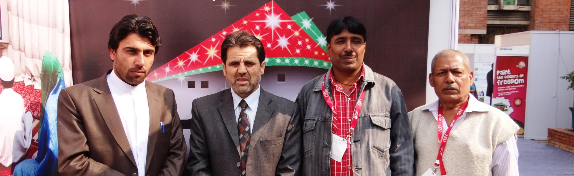 A group photo featuring DOP Avinash Kumar and an Afghan client standing before a colorful 'Paint the Colours of Freedom' backdrop during a video production event in Delhi. film shooting locations in india, video shooting locations in india, tv shooting locations in india, shooting locations in india