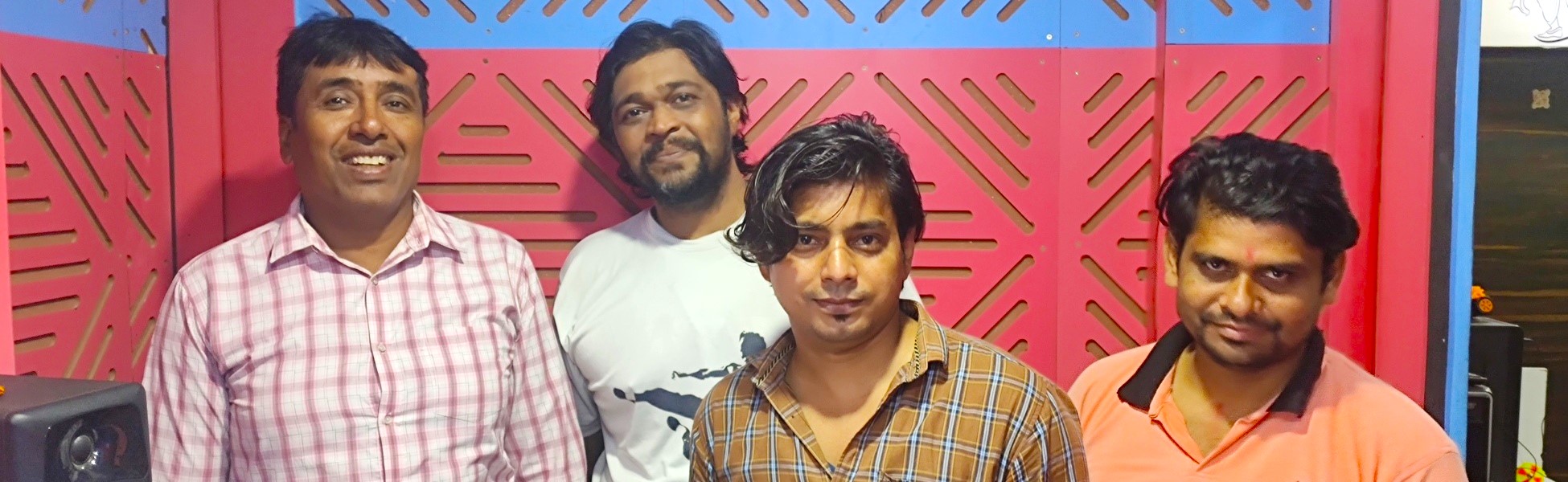 Four men, including a voice-over artist and sound engineer, posing together inside a professional audio recording studio in New Delhi. fixer in Nawada, line producer in Nawada