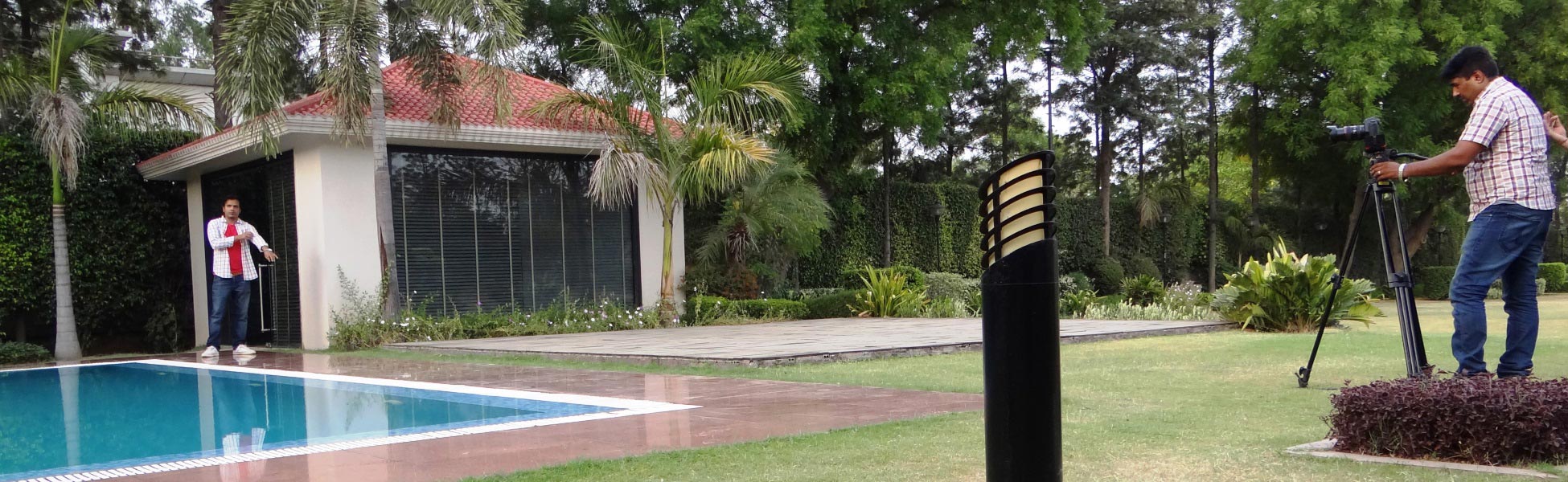 Trisna Films® production crew filming a music video on location in New Delhi, India; featuring a videographer with a tripod-mounted camera capturing talent by a luxury poolside villa. film shooting locations in Ariyalur, video shooting locations in Ariyalur, tv shooting locations in Ariyalur, shooting locations in Ariyalur
