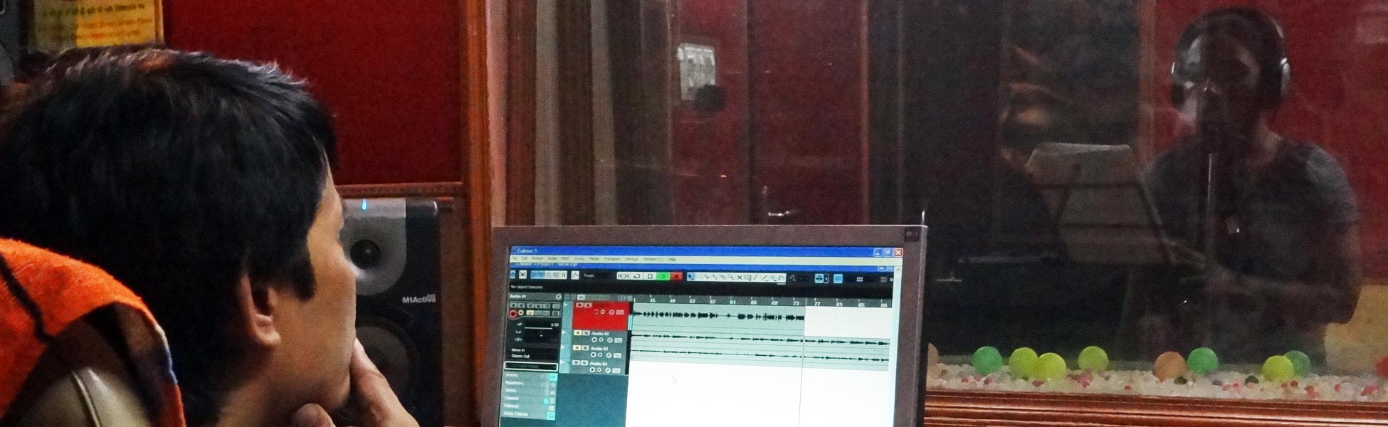 Trisna Films® professional audio engineer monitoring a vocal recording session at an audio studio in New Delhi, India, with a voice-over artist visible in the recording booth. film shooting locations in india, video shooting locations in india, tv shooting locations in india, shooting locations in india