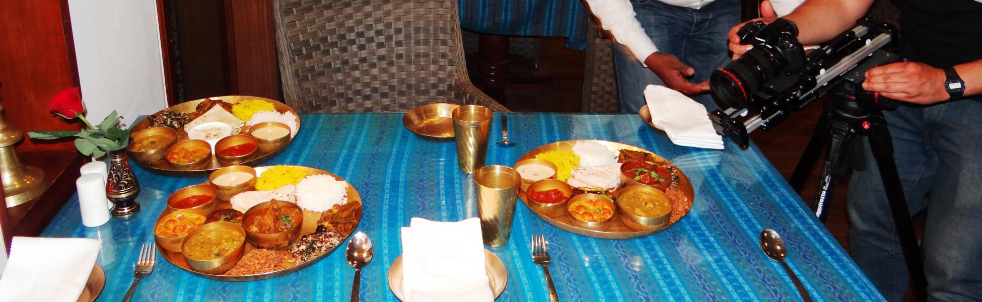A professional camera setup on a tripod filming three traditional Odia thali meals served in authentic brass plates on a blue tablecloth, showcasing the rich culinary heritage of Odisha, India. film shooting locations in Bagalkot, video shooting locations in Bagalkot, tv shooting locations in Bagalkot, shooting locations in Bagalkot