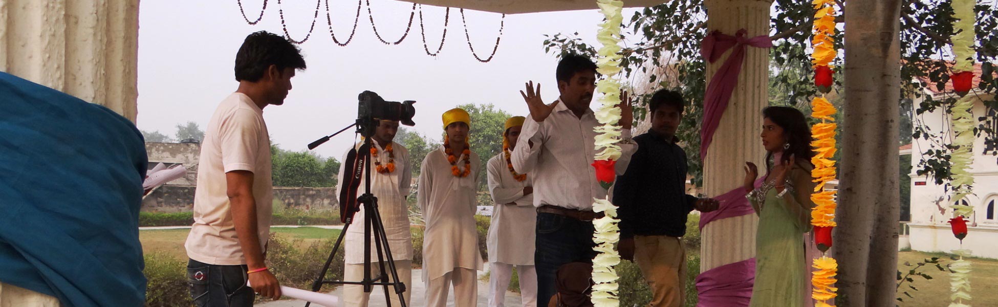 Behind-the-scenes shot of a director gesturing to actors on an outdoor film set in Delhi, India, for the short film 'Andhvishwas'. A professional camera on a tripod is positioned in the foreground while actors in traditional yellow turbans wait for cues. film production house in Bageshwar, video production house in Bageshwar, tv production house in Bageshwar, production house in Bageshwar, film production company in Bageshwar, video production company in Bageshwar, tv production company in Bageshwar, production company in Bageshwar