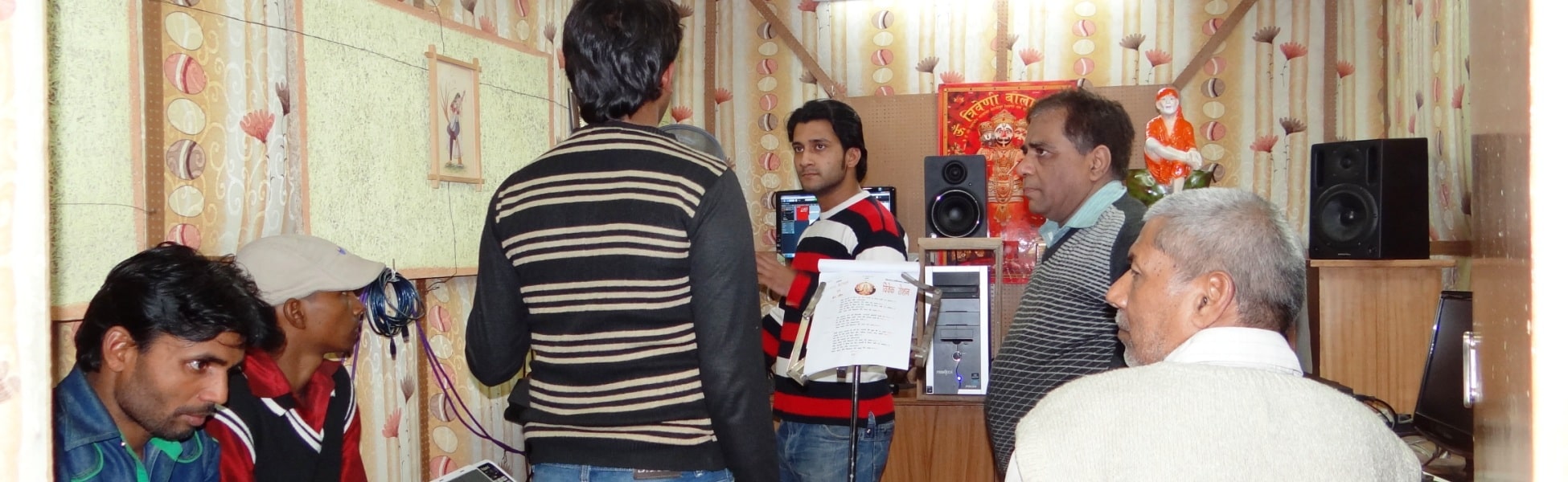 A group of music producers and artists collaborating inside a small digital audio recording studio in Delhi, featuring studio monitors, a computer screen running a DAW, and a lyric sheet stand. film production house in Ballia, video production house in Ballia, tv production house in Ballia, production house in Ballia, film production company in Ballia, video production company in Ballia, tv production company in Ballia, production company in Ballia