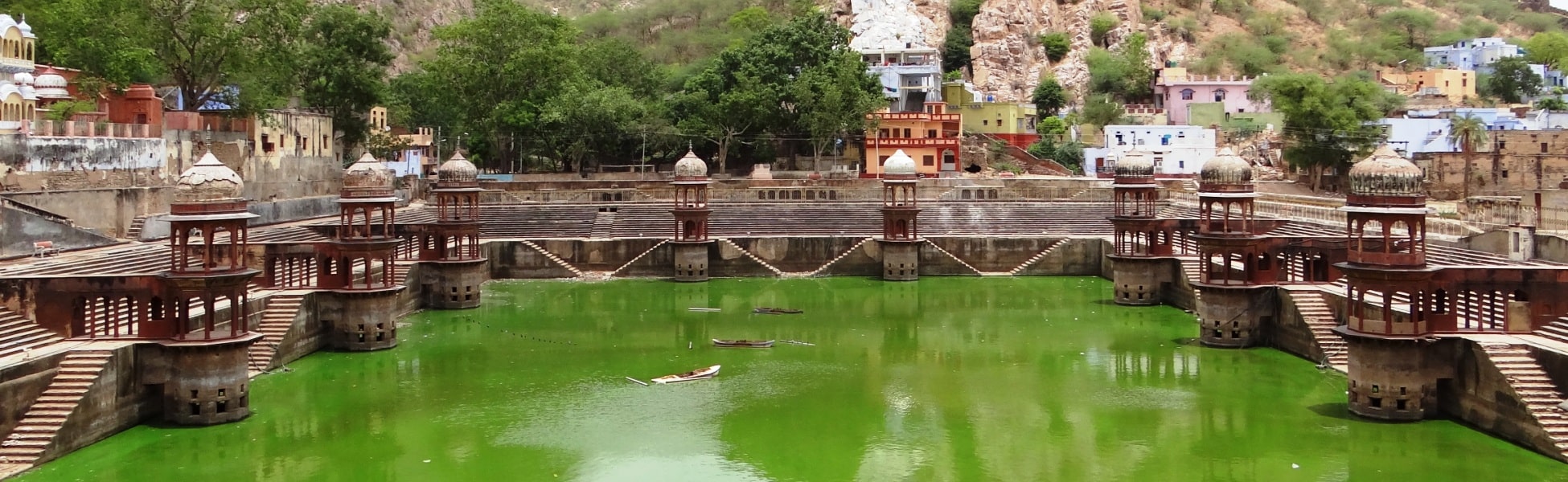 Panoramic wide shot of Sagar Kund step-pond in Alwar, Rajasthan, featuring symmetrical red sandstone chhatris (cenotaphs) along the emerald green water, situated below the Aravalli hills and adjacent to Moosi Maharani ki Chhatri. film shooting locations in Ballia, video shooting locations in Ballia, tv shooting locations in Ballia, shooting locations in Ballia